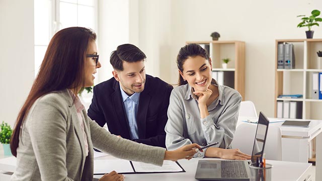 a businesswoman presenting information on a laptop to a smiling couple in an office